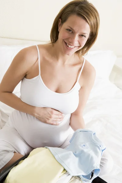 Mujer embarazada empacando ropa de bebé en maleta sonriendo —  Fotos de Stock