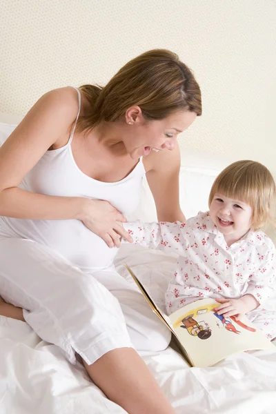 Pregnant woman in bedroom reading book with daughter laughing — Stock Photo, Image