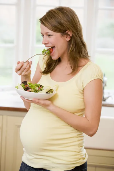 Mujer embarazada en la cocina comiendo una ensalada sonriendo —  Fotos de Stock