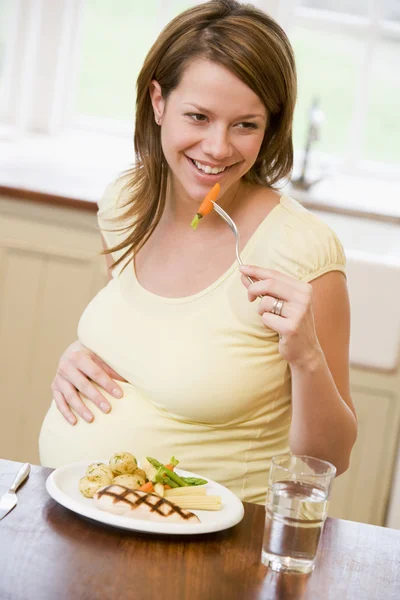 怀孕的女人在厨房里吃鸡肉和蔬菜微笑 — 图库照片