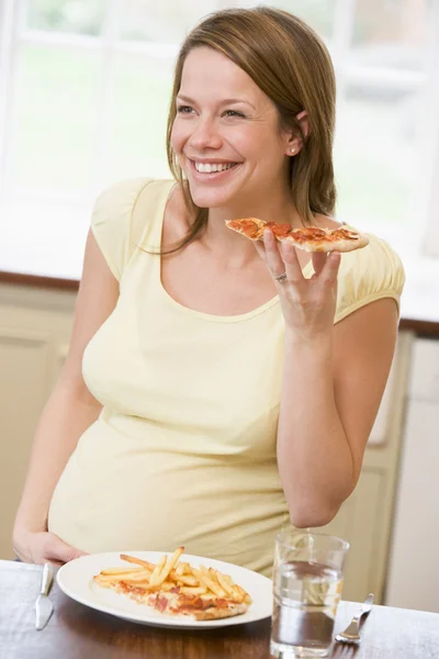 怀孕的女人在厨房里吃薯条和比萨微笑 — 图库照片
