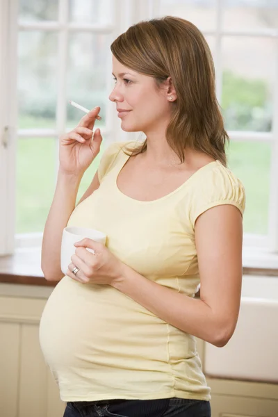 Těhotná žena, která stála v kuchyni s kávou a cigaretou — Stock fotografie
