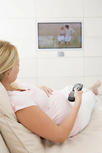 Mulher grávida assistindo televisão usando controle remoto — Fotografia de Stock