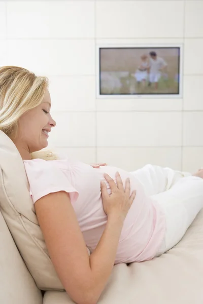 妊娠中の女性は笑みを浮かべてテレビを見て — ストック写真