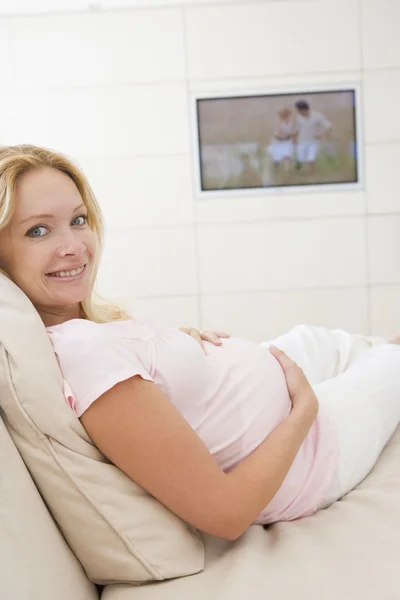 Mujer embarazada viendo la televisión sonriendo —  Fotos de Stock
