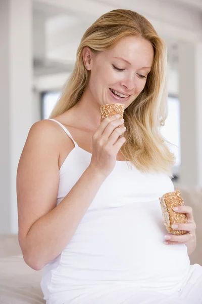 Беременная женщина ест хлеб и улыбается — стоковое фото