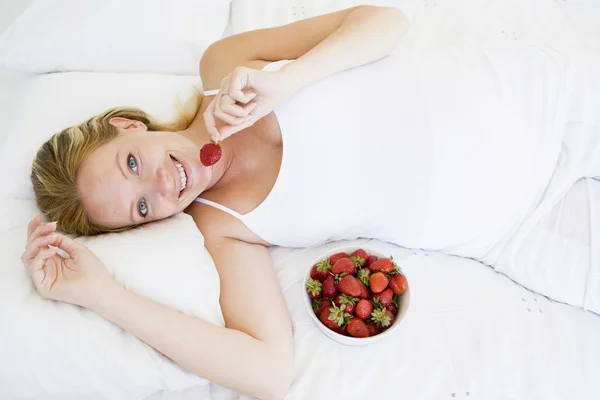 Schwangere liegt mit Schale voller Erdbeeren im Bett und lächelt — Stockfoto