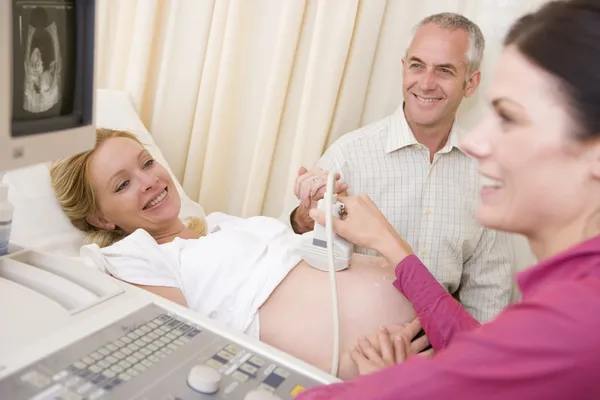 Mulher grávida recebendo ultra-som do médico com o marido assistir — Fotografia de Stock