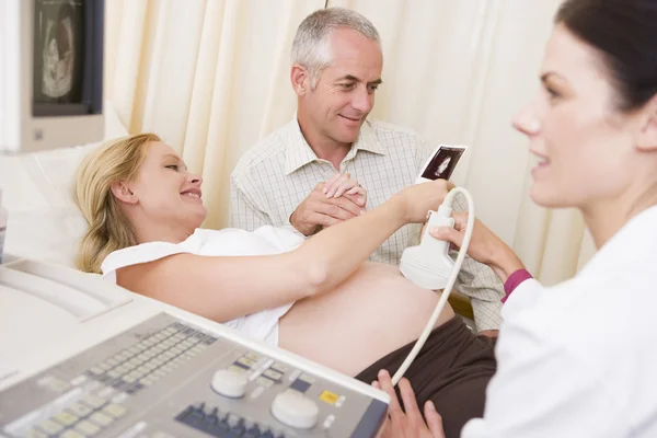 Pregnant woman getting ultrasound from doctor with husband looki — Stock Photo, Image