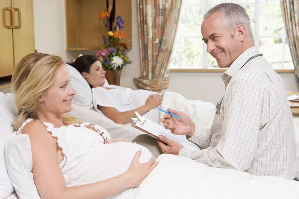 グラフを保持していると笑みを浮かべて妊娠中の女性に話す医師 — ストック写真