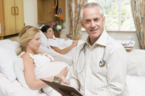 Lekarz siedzi przez kobiety w ciąży, trzymając wykresu i uśmiechając się — Zdjęcie stockowe