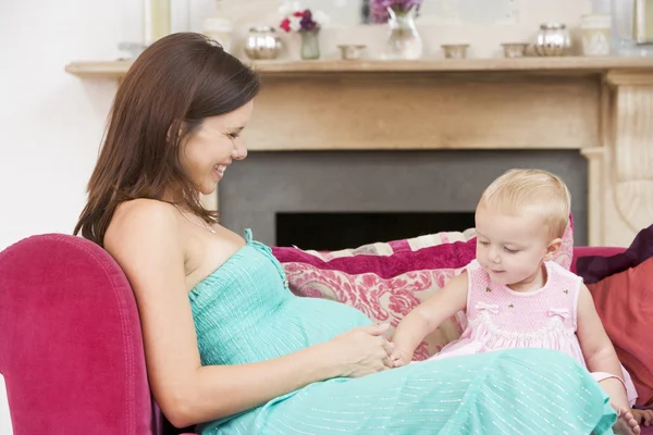 Madre incinta con figlia in soggiorno toccando pancia e — Foto Stock