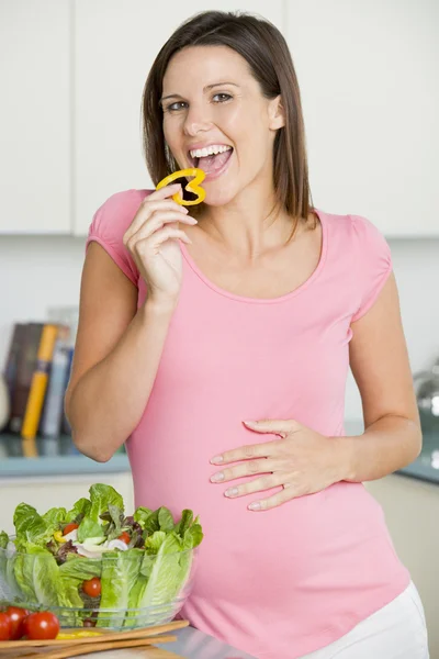 Беременная женщина на кухне делает салат и улыбается — стоковое фото