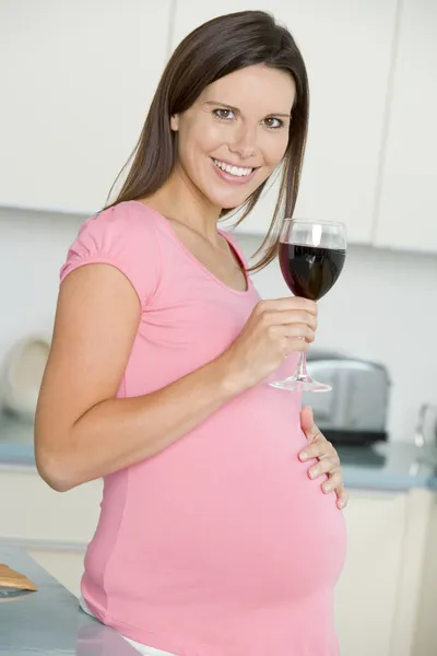 怀孕的女人在厨房里与玻璃的红酒笑 — 图库照片