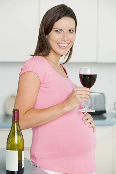 Беременная женщина на кухне с бокалом красного вина улыбается — стоковое фото