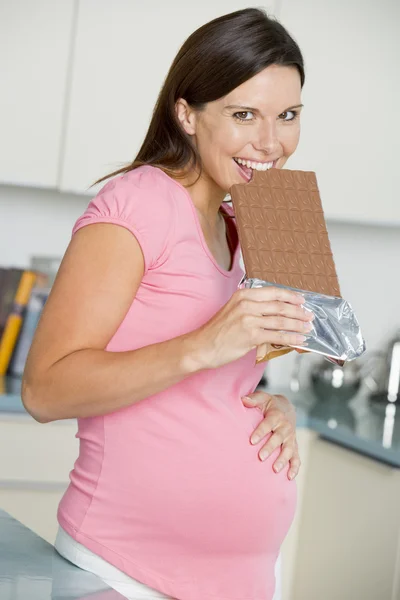 Pregnant woman in kitchen with large chocolate bar smiling — Stock Photo, Image