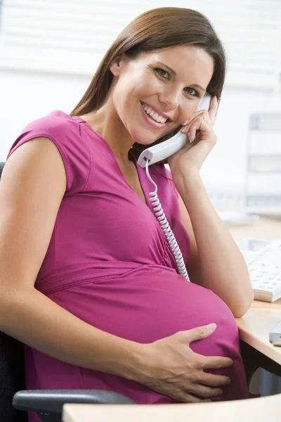 Hamile kadın gülümseyerek telefon kullanarak iş başında — Stok fotoğraf
