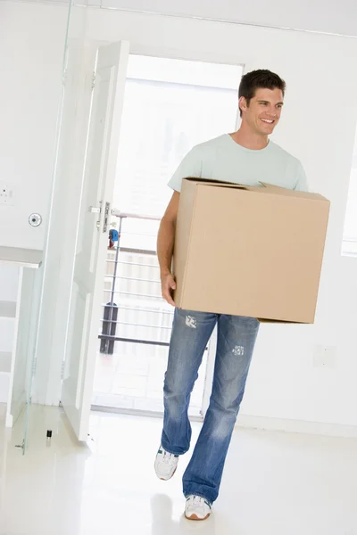 Человек с коробкой переезжает в новый дом улыбаясь — стоковое фото