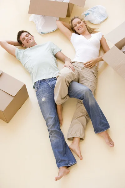 Casal deitado no chão por caixas abertas em nova casa sorrindo — Fotografia de Stock