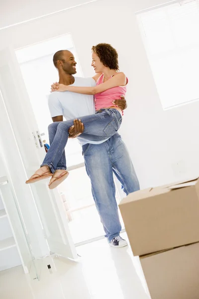 Муж держит жену в новом доме, улыбаясь — стоковое фото