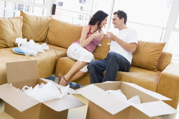 Casal relaxante com champanhe por caixas em nova casa sorrindo — Fotografia de Stock