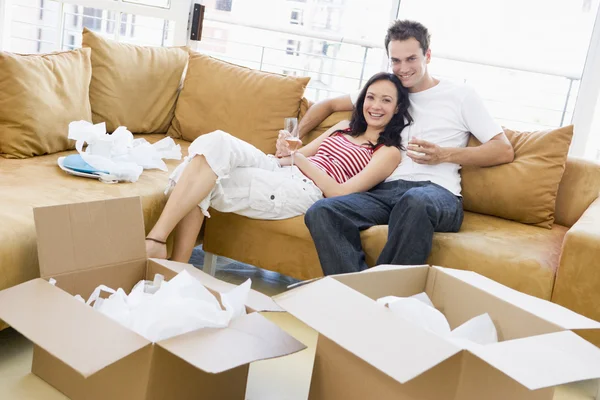 Casal relaxante com champanhe por caixas em nova casa sorrindo — Fotografia de Stock