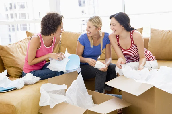 Tre amici ragazza disimballaggio scatole in nuova casa sorridente — Foto Stock