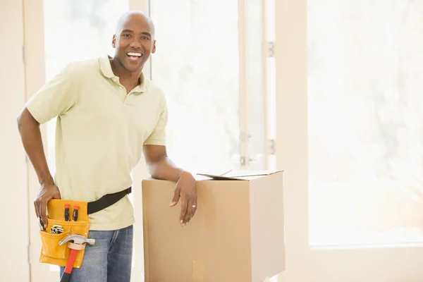 Homem usando cinto de ferramentas em pé por caixas em nova casa sorrindo — Fotografia de Stock