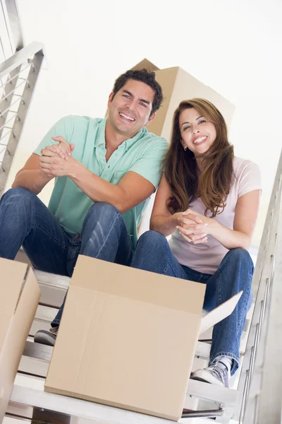 Coppia seduta su scala con scatole in nuova casa sorridente — Foto Stock
