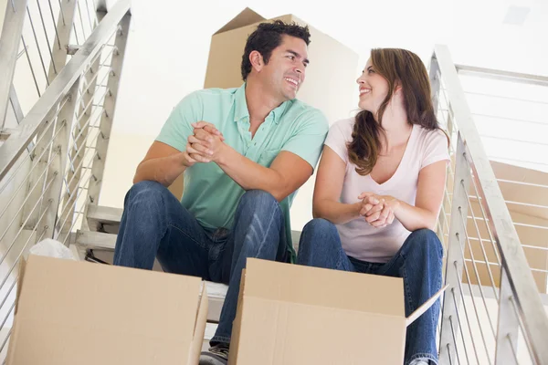 Пара сидить на сходах з коробками в новому будинку посміхається — стокове фото