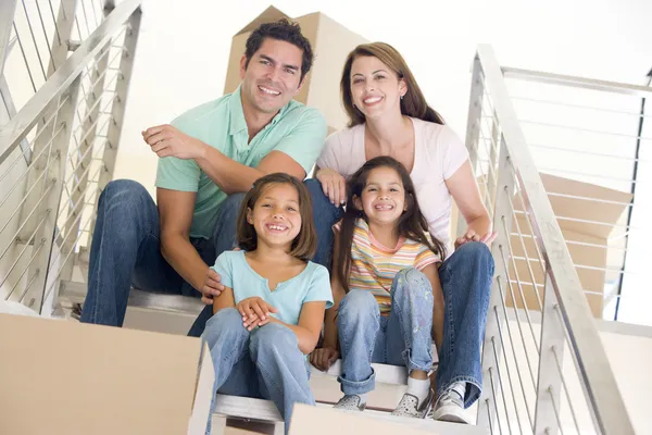 Семья сидит на лестнице с коробками в новом доме улыбаясь — стоковое фото