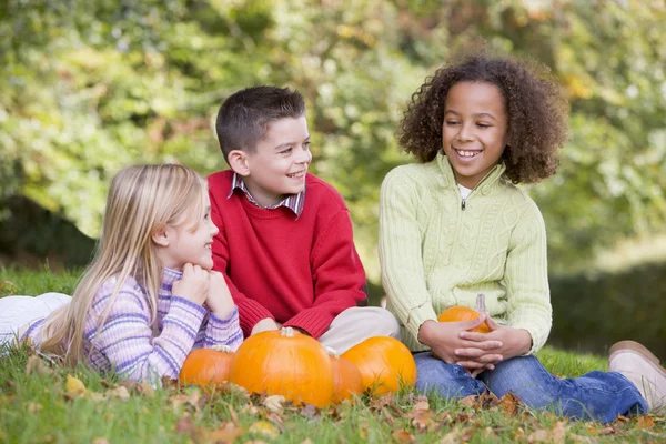 Tre Giovani Amici Seduti Sull Erba Con Zucche Sorridenti — Foto Stock
