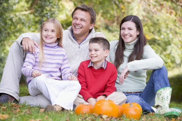 Família sentada na grama com abóboras sorrindo — Fotografia de Stock