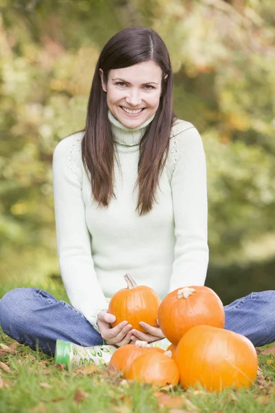 Mujer sentada en la hierba con calabazas sonriendo —  Fotos de Stock