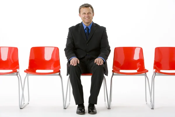 Бизнесмен, сидящий в ряду пустых стульев — стоковое фото