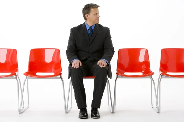 Uomo d'affari seduto in fila di sedie vuote — Foto Stock