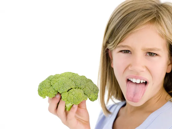 Молодая девушка держит брокколи и высовывает язык — стоковое фото