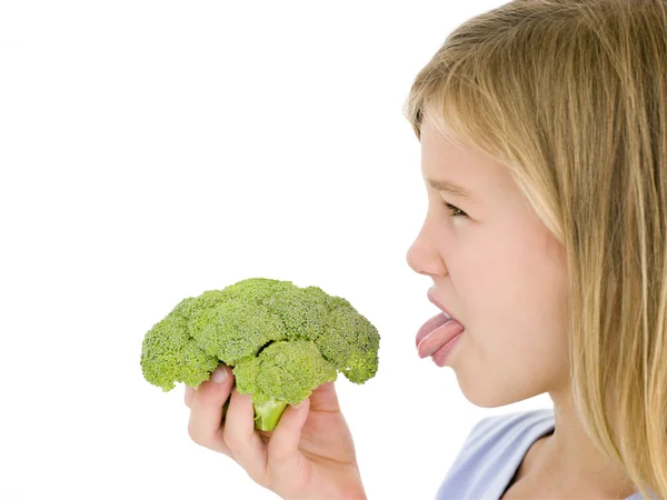 Young girl holding broccoli and sticking tongue out — Stock Photo, Image