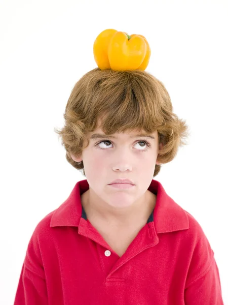 顔をしかめ彼の頭の上に黄色の唐辛子の少年 — ストック写真