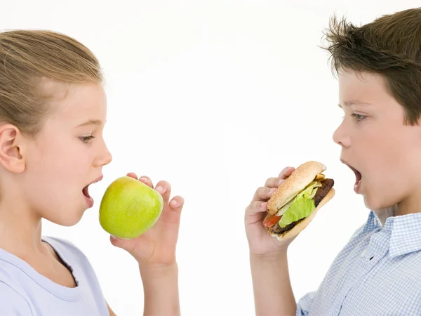 Hermana comiendo manzana por hermano comiendo hamburguesa con queso —  Fotos de Stock