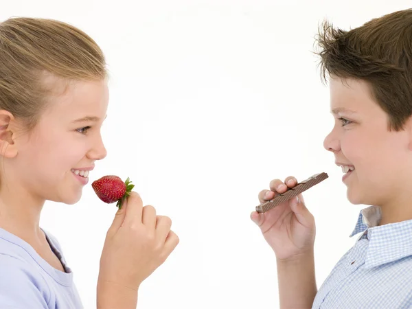 Сестра їсть полуницю за братом їсть шоколадний батончик — стокове фото
