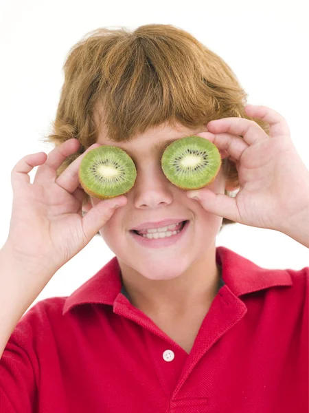 Jovem menino segurando kiwi metades sobre os olhos sorrindo — Fotografia de Stock
