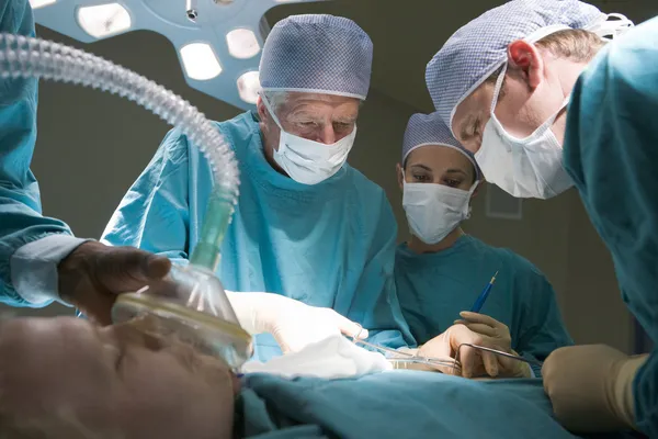 Três cirurgiões operando em um paciente — Fotografia de Stock