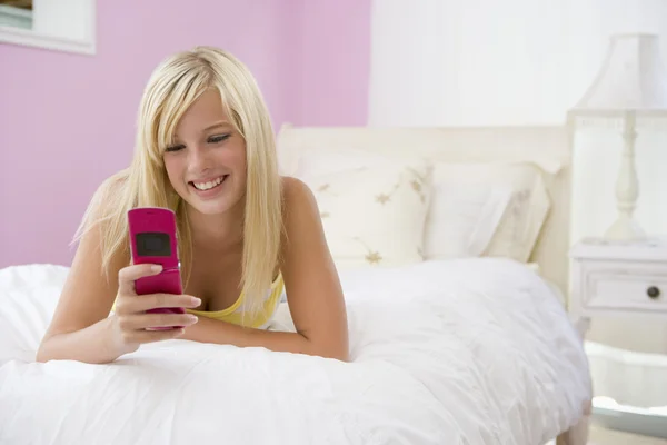 Menina adolescente deitada na cama usando o telefone móvel — Fotografia de Stock
