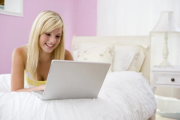 Dizüstü bilgisayar kullanan yatakta yatarken genç kız — Stok fotoğraf