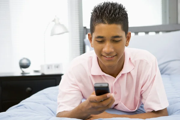 十几岁的男孩躺在床上使用的移动电话上 — 图库照片