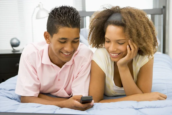Adolescentes acostados en la cama juntos mirando el teléfono móvil —  Fotos de Stock