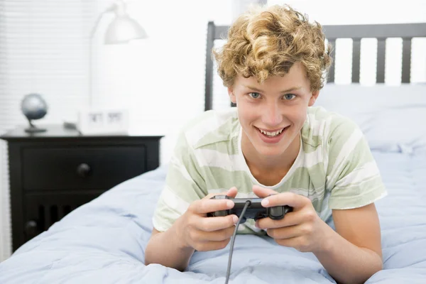Tonårspojke liggande på sängen spelar videospel — Stockfoto