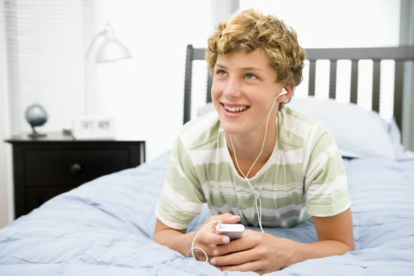 十几岁的男孩躺在床上听 mp3 播放器 — 图库照片
