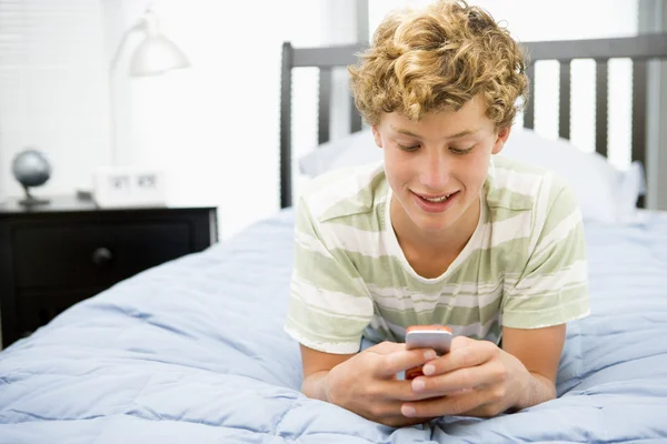Cep telefonu kullaranarak yatakta yatarken genç çocuk — Stok fotoğraf